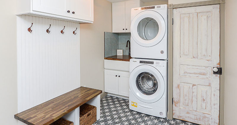 mudroom laundry area with hangers, cabinets, convertible utility sink, and bench with stowaway totes