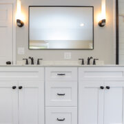 A bathroom with a white double-sink vanity, one mirror, and wall sconce lights