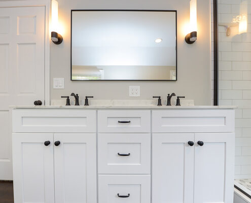 A bathroom with a white double-sink vanity, one mirror, and wall sconce lights