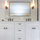 A bathroom with a white double-sink vanity, one mirror, and wall sconce lights